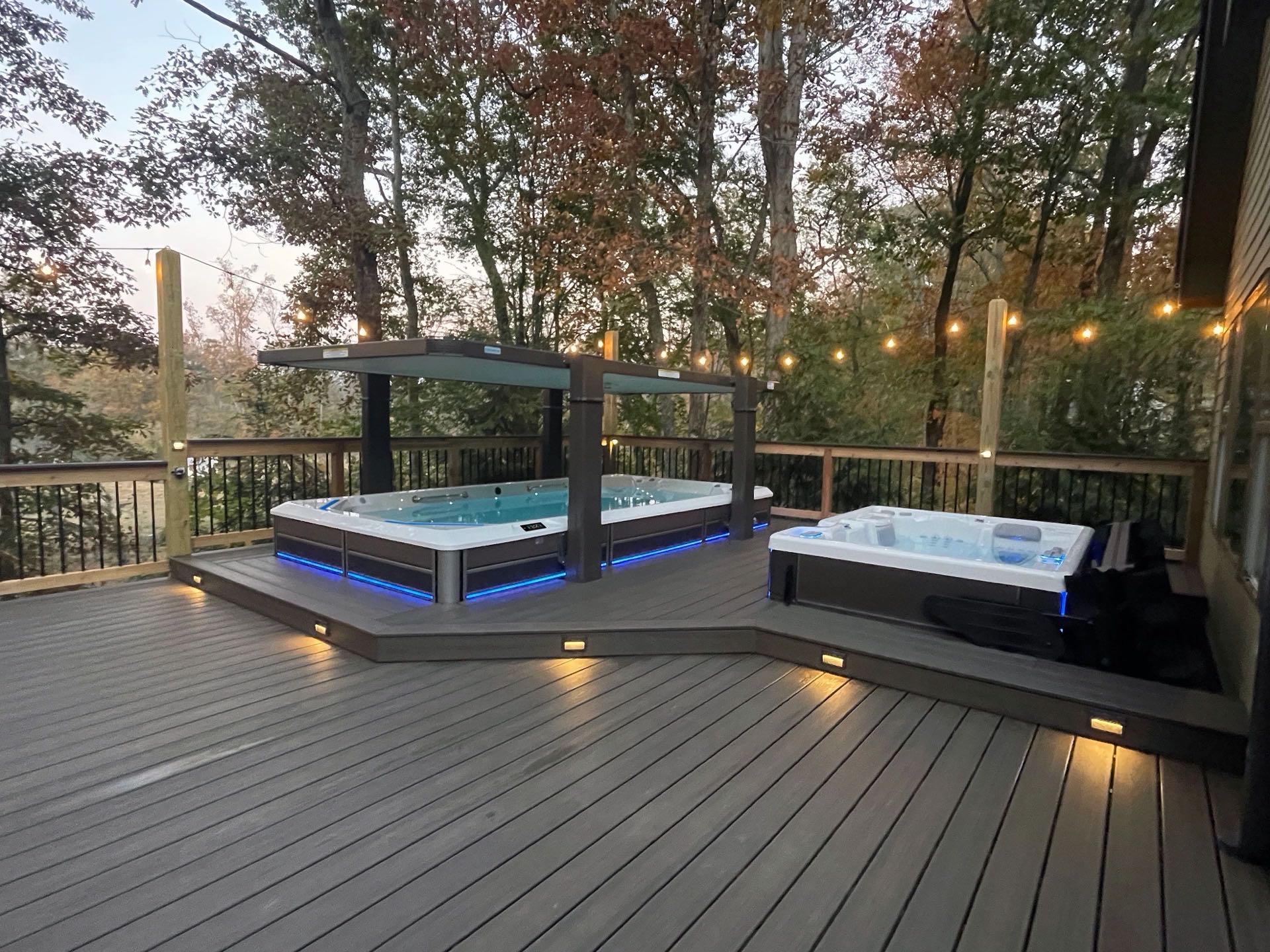 Swim spa and hot tub on a deck at dusk with string lights